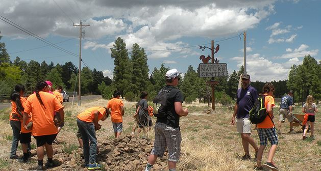 People Wearing Orange T-Shirts Gathered Working on a Project by Nature Center Sign