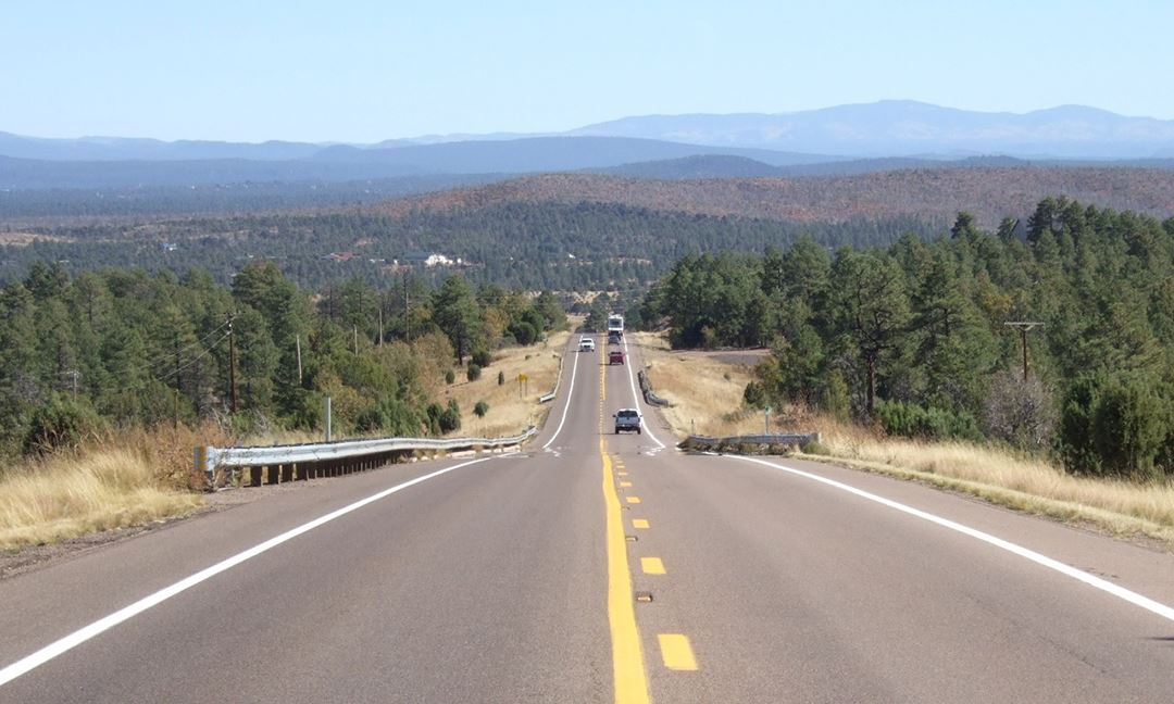Vehicles Driving on the Highway, Fir Trees on Either Side and Mountains Beyond