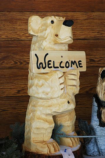 Wooden Statue of a Small Bear Holding a Welcome Sign