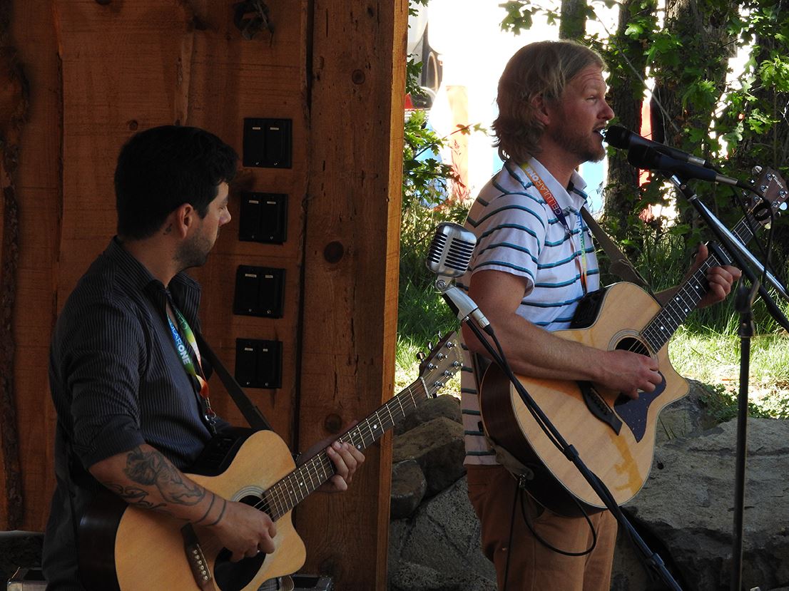 Two Men Playing Guitars, One Singing into Microphone
